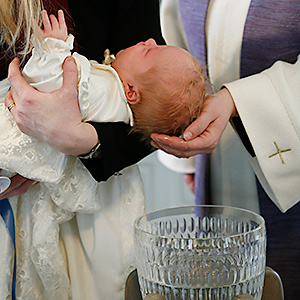 Vauva kastemekossa kastemaljan yläpuolella, papin käsi pitelee vauvan päätä.