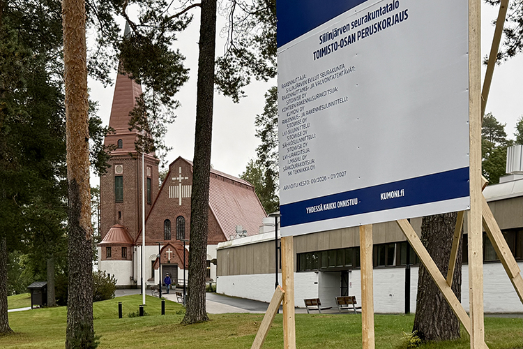 Seurakuntatalon pihalla oleva remonttikyltti, taustalla häämöttää kirkko