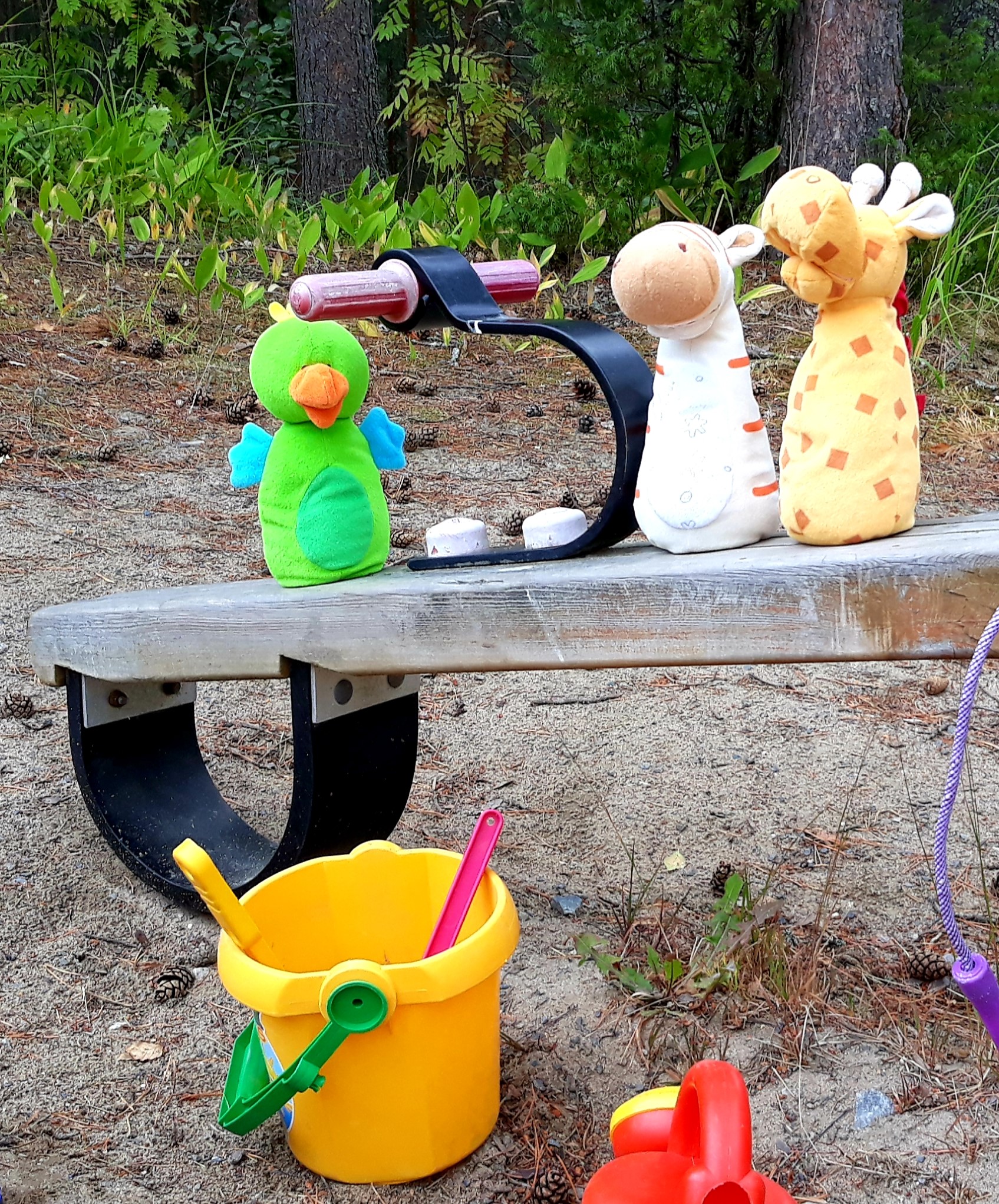 Puistokerho Pehmolelut leikkipuiston kiikkulaudalla. Kiikkulaudan alla hiekkaleluja.