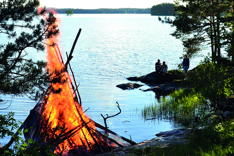 Perinteiset juhannusjuhlat Ruokoniemessä juhannuskokko Ruokoniemessä, ihmisiä istumassa rannalla