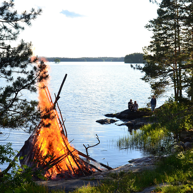 rannalla ihmisiä ja juhannuskokko
