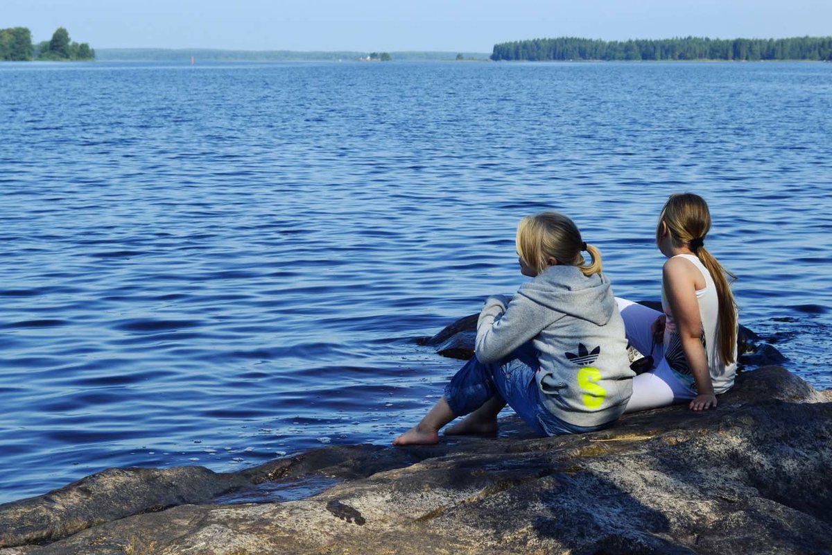 Kaksi tyttöä istuu kesällä rantakalliolla.