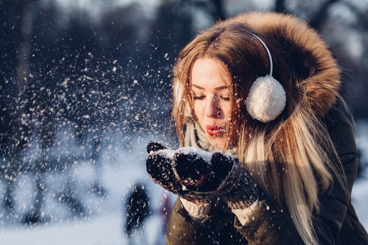 Nuori nainen ulkona talvella, puhaltaa kädeltään lunta ilmaan.