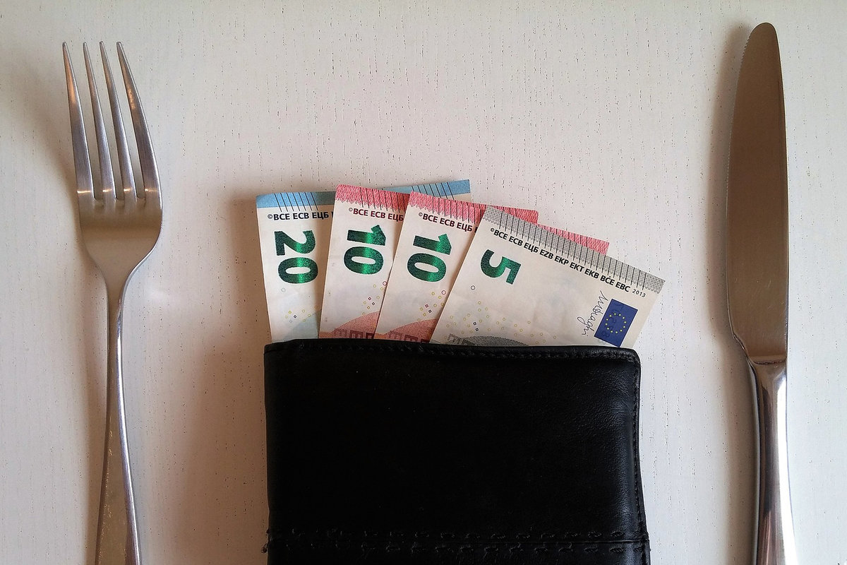 Rahapussi, haarukka ja veitsi pöydällä. Rahapussista näkyy setelirahoja.