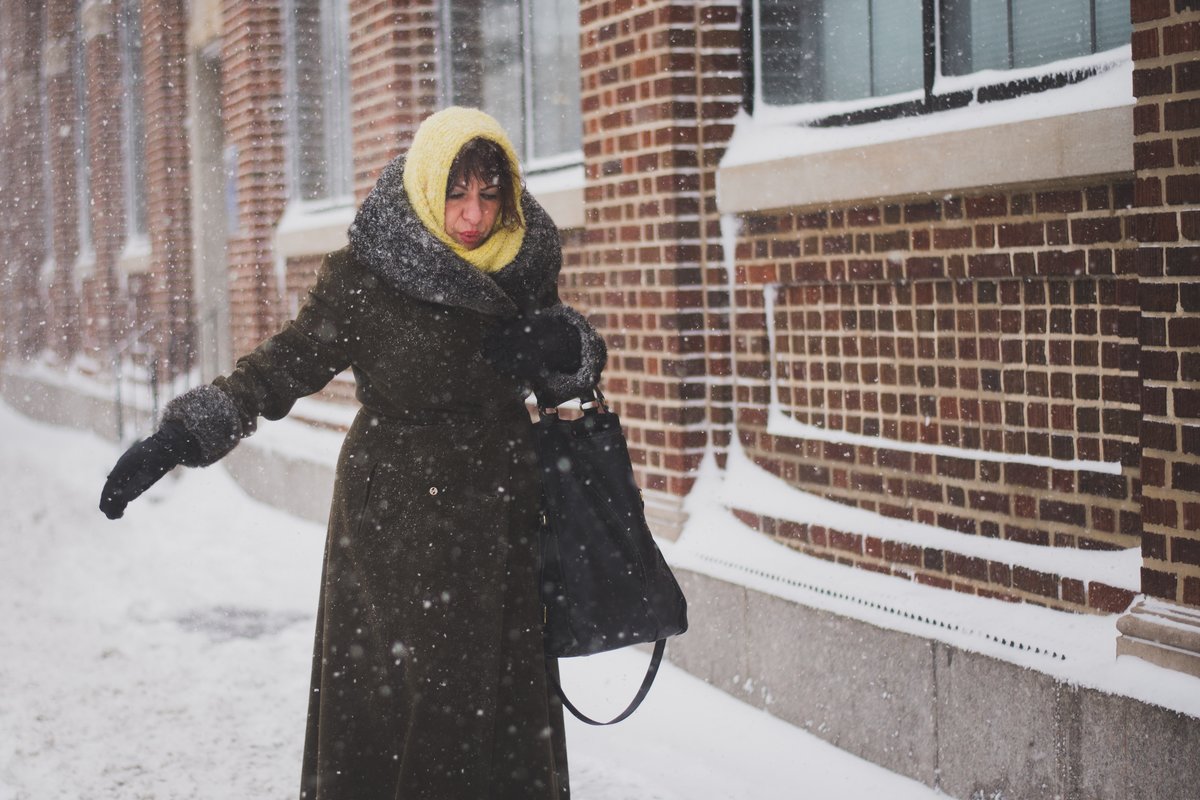 Lämpimästi pukeutunut nainen kävelee talvisella kadulla tiilitalon seinustalla.