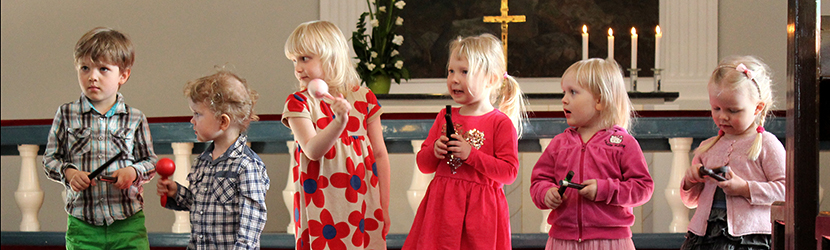 Kuusi pikkulasta soittaa kirkossa marakasseja ja kapuloita.
