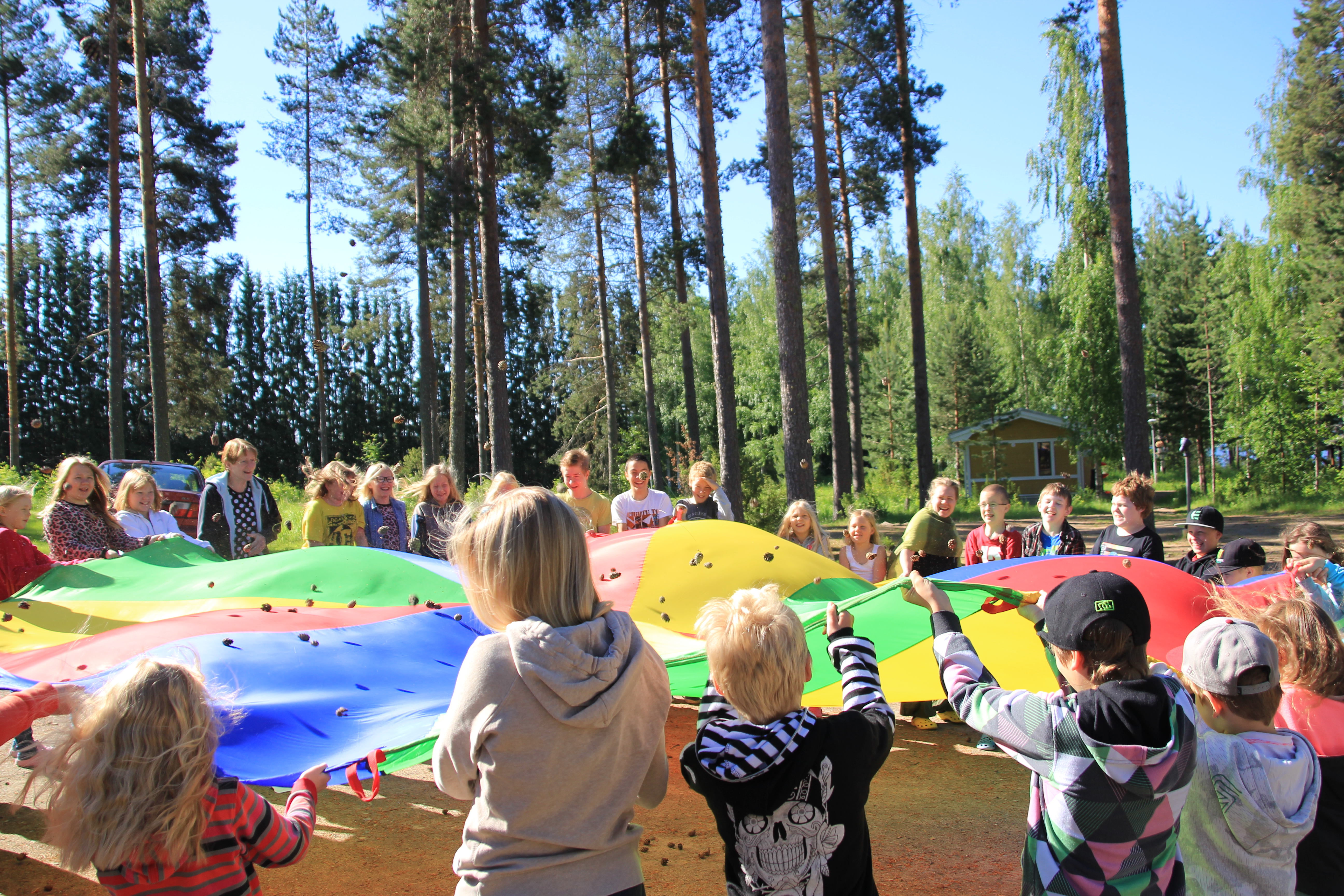 Lapset leikkivät leikkivarjolla leirikeskuksen pihassa.