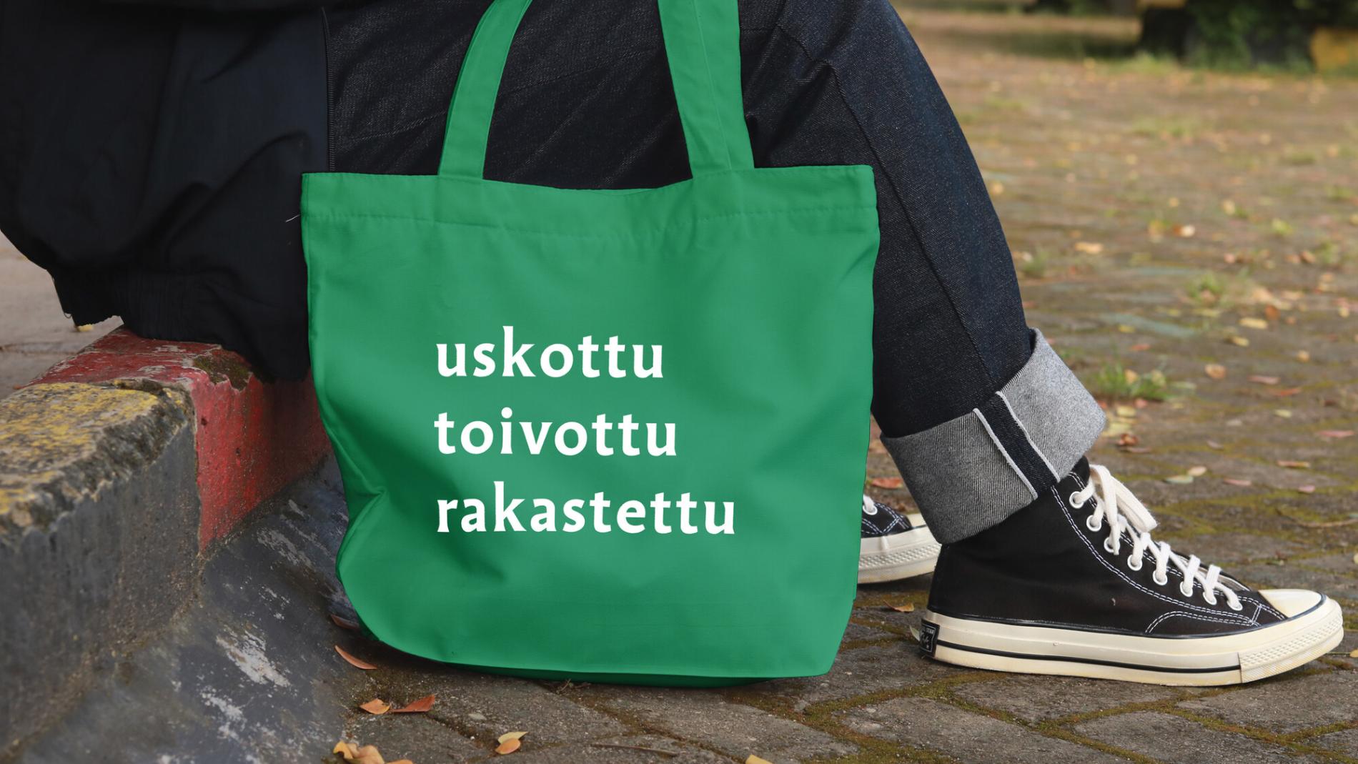 Henkilö istuu ulkona, näkyvissä uskottu, toivottu, rakastettu -kassi ja jalat, joissa on koripallotossut.
